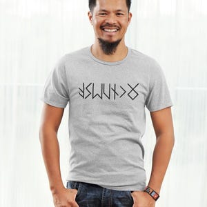 A man wearing a gray t-shirt with a graphic design and smiling at the camera.