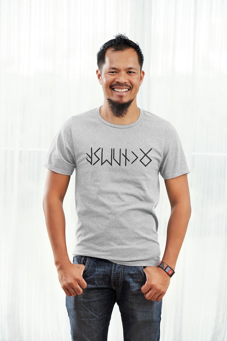 A man wearing a gray t-shirt with a graphic design and smiling at the camera.