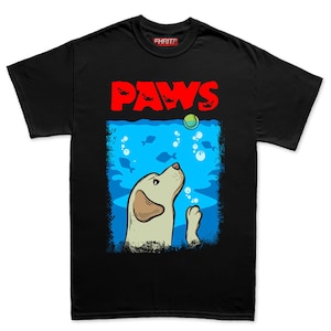 May include: Black t-shirt with a graphic featuring a yellow Labrador Retriever looking up at a tennis ball. The word "PAWS" is in red block letters above the dog, with fish illustrations. The dog is in a blue underwater scene.