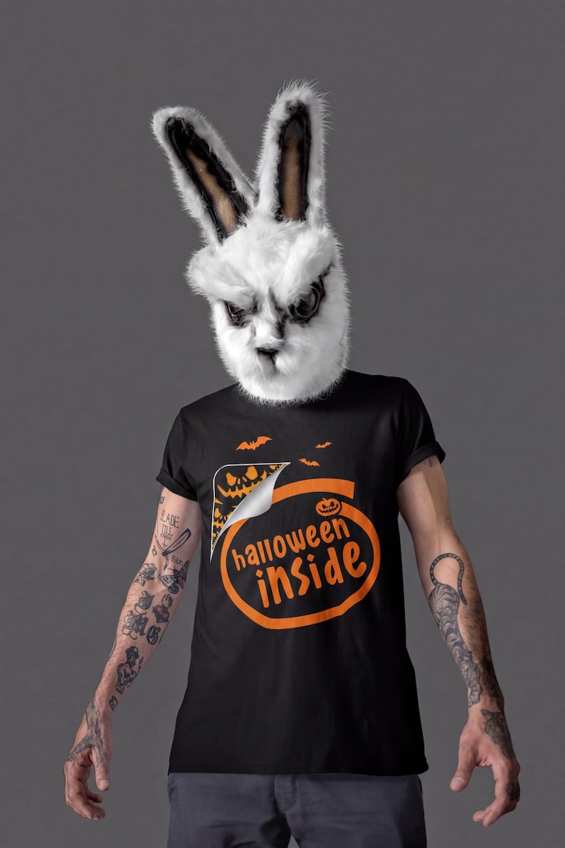 A person wearing a bunny mask and a Halloween-themed t-shirt stands against a gray background.