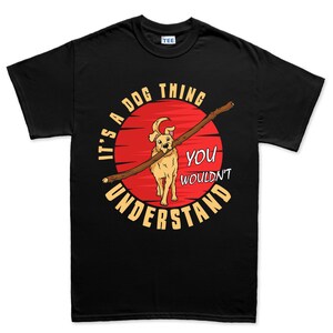 May include: Black t-shirt with a graphic of a dog carrying a stick, set against a red circle resembling a sunset. The text reads "IT'S A DOG THING YOU WOULDN'T UNDERSTAND" in white and yellow lettering. A "TEE" tag is visible.