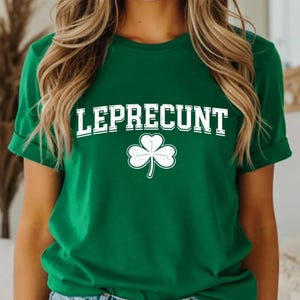 A woman wearing a green t-shirt with the word "LEPRECIUT" printed on it, standing in front of a mirror.