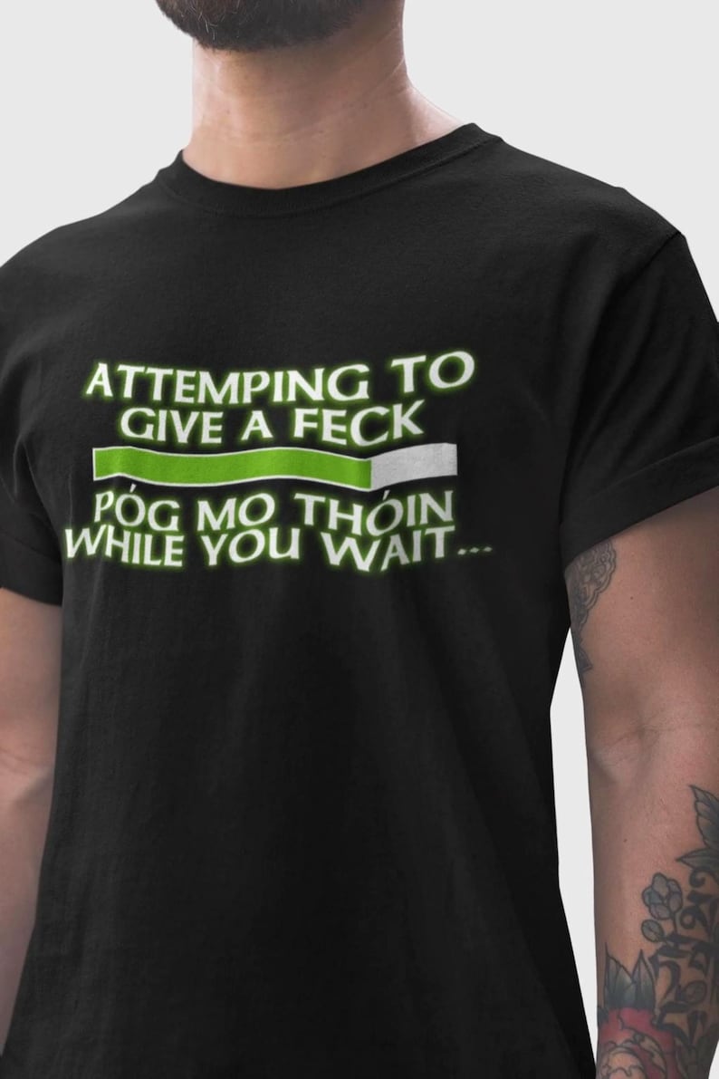 A black t-shirt with white text that reads "ATTEMPTING TO GIVE A FEK POG MO THION WHILE YOU WAIT..."