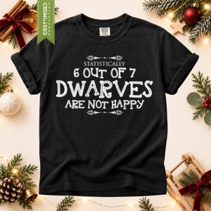 Op de afbeelding: Een zwart t-shirt met korte mouwen en witte tekst die luidt Statistically 6 out of 7 Dwarves are not happy. Het shirt heeft een ronde hals en een standaard pasvorm, met de afbeelding gecentreerd op de borst in een decoratief lettertype.