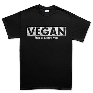 May include: Black t-shirt with the word "VEGAN" in a distressed white font, above the phrase "just to annoy you". The shirt has a crew neck and short sleeves. The tag on the collar reads "TEE".