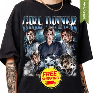 May include: A black short-sleeve t-shirt featuring a graphic print of five identical male characters with light brown hair, each wearing dark tactical gear. The text GIRL DINNER is printed in a metallic blue font above the character collage.