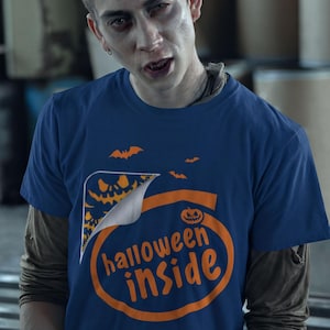 A man wearing a blue t-shirt with the text "Halloween inside" printed on it, looking directly at the camera with a serious expression.