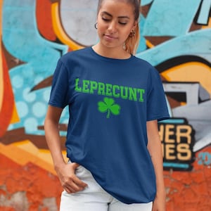 A young woman wearing a blue t-shirt with the word "Leprecht" printed on it, standing in front of a colorful graffiti wall.