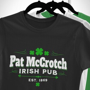 A black t-shirt with white text and green shamrocks hanging on a clothing rack.