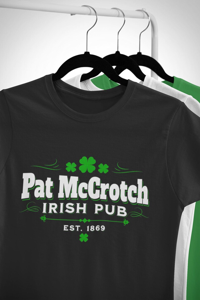 A black t-shirt with white text and green shamrocks hanging on a clothing rack.