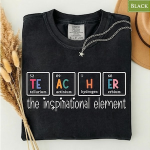 Peut inclure: Un t-shirt noir avec un graphique de tableau périodique épelant TEACHER en utilisant les éléments Tellurium, Actinium, Hydrogen et Erbium. Sous le graphique, le texte indique the inspirational element dans une police blanche manuscrite.