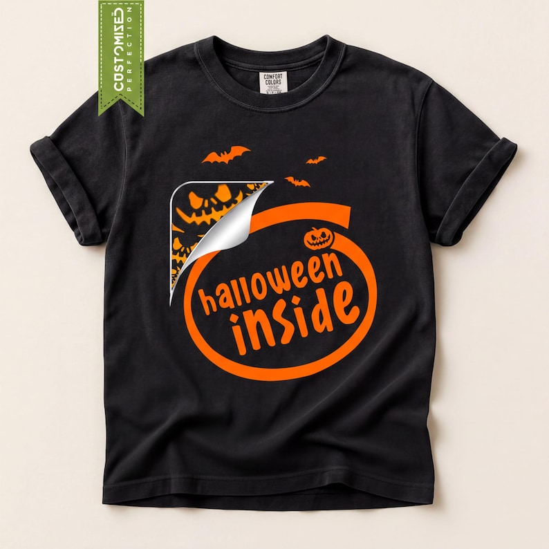 A black t-shirt with a Halloween-themed graphic design, including a bat silhouette, a pumpkin, and the text "Halloween inside".