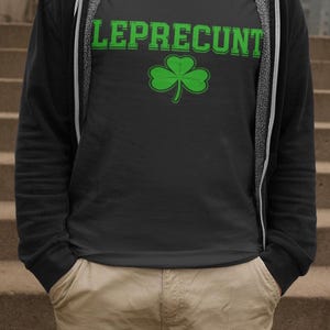 A person wearing a black t-shirt with the text "LEPRECIUNT" and a green shamrock graphic, standing on a set of stairs.