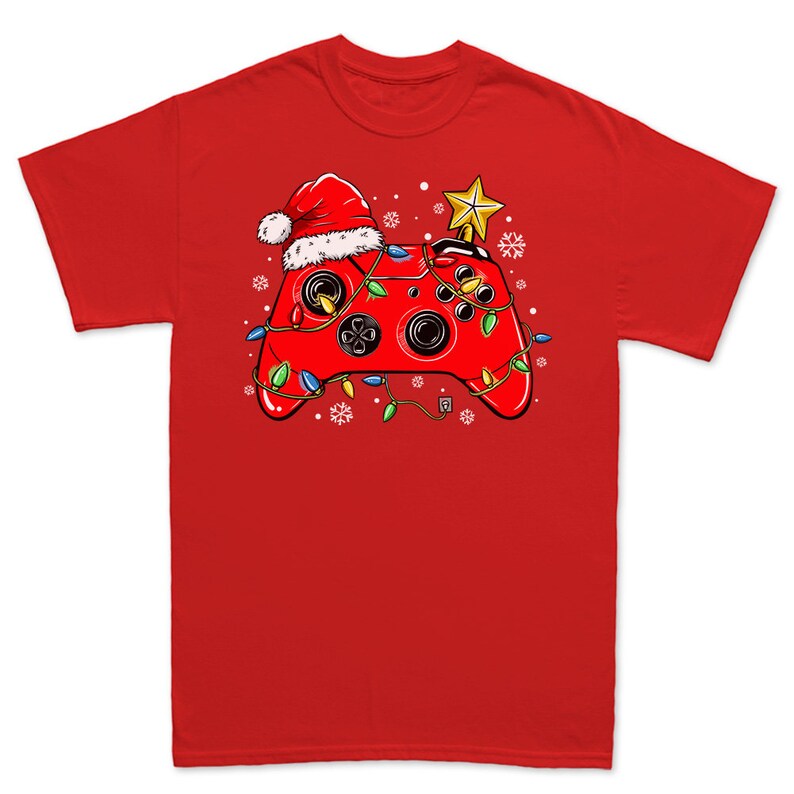 K&ouml;nnte beinhalten: Rotes T-Shirt mit einem Weihnachts-Videospiel-Controller-Design. Der Controller ist mit einem Weihnachtsmann-Hut, Weihnachtslichtern und einem Stern obenauf verziert.