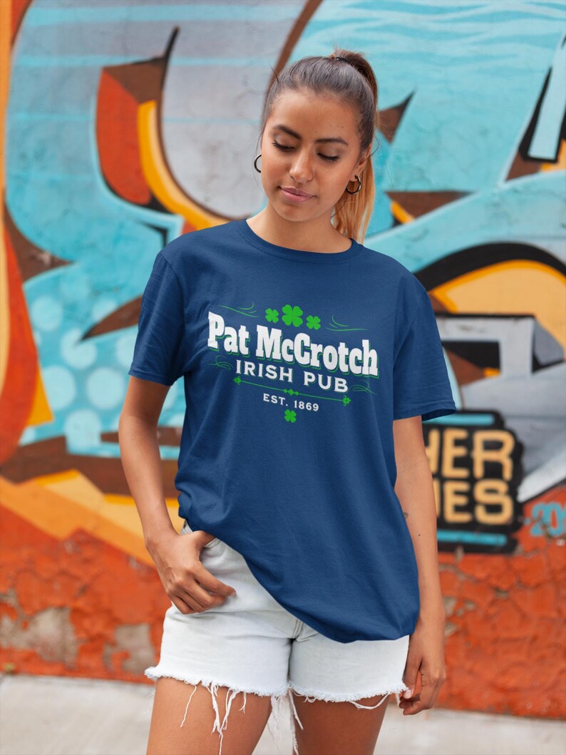 A woman wearing a blue t-shirt with the text "Pat Groth Irish Pub EST.1869" stands in front of a colorful graffiti wall.