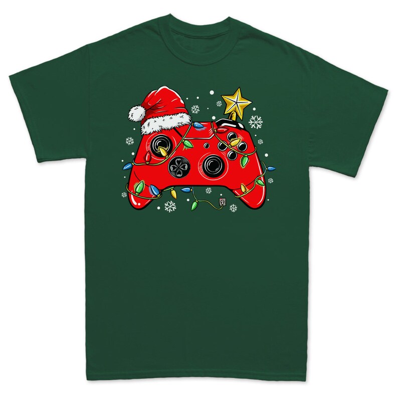 K&ouml;nnte beinhalten: Ein gr&uuml;nes T-Shirt mit einem roten Videospiel-Controller, der einen Weihnachtsmann-Hut und Weihnachtslichter tr&auml;gt. Der Controller ist mit einem Stern oben drauf verziert.