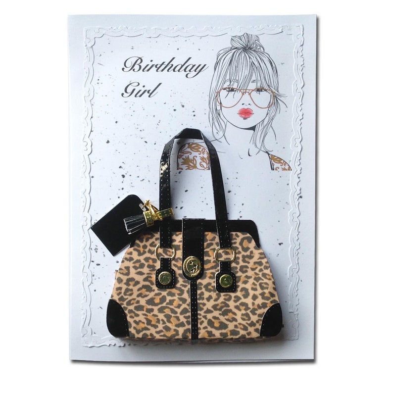 Op de afbeelding: Een verjaardagskaart met een zwart en bruin handtasje met luipaardprint met gouden accenten en een zwart en gouden kwastje. De kaart heeft de tekst "Birthday Girl" erop.
