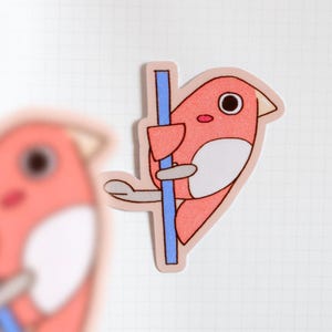 May include: A sticker featuring a cartoon bird in shades of coral and white, perched on a blue pole. The bird has a large eye and is outlined in a darker coral color. The sticker is on a white, grid-lined surface.
