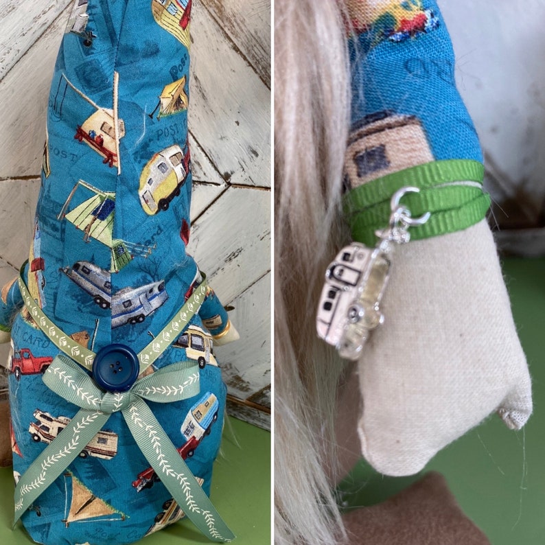 May include: A blue gnome with a white beard and a green ribbon around its waist. The gnome is wearing a blue and white fabric with a pattern of campers and tents. The gnome is holding a silver charm of a camper.