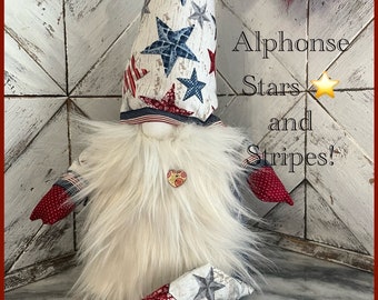 May include: A white, red, and blue gnome with a star-patterned hat and red and white polka dot pants. The gnome is sitting on a white surface. The text "Alphonse Stars and Stripes" is written on the image.