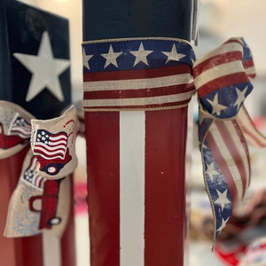 May include: Two red, white, and blue wooden blocks with a white star on one block and a red, white, and blue ribbon tied around the other block.