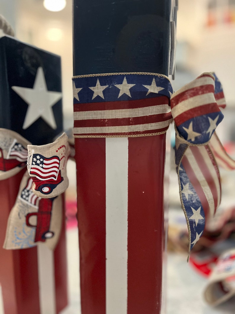 May include: Two red, white, and blue wooden blocks with a white star on one block and a red, white, and blue ribbon tied around the other block.
