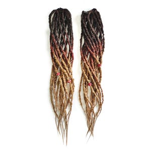 Puede incluir: Dos juegos de rastas sintéticas ombré con tonos negros, rojos y rubios. Las rastas tienen cuentas rojas y miden aproximadamente 61 cm de largo.