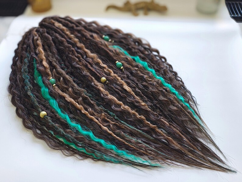 May include: Brown and blonde synthetic dreadlocks with turquoise accents and gold beads. The dreadlocks are wavy and long.