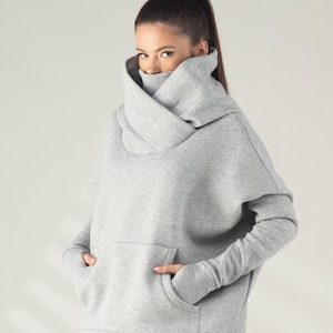 Op de afbeelding: Lichtgrijze trainingspak bestaande uit een hoodie met een col en bijpassende joggingbroek. De persoon draagt rode, zwarte en witte sneakers. De outfit is casual en comfortabel.