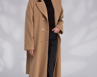 May include: A long, camel-colored coat with a classic design. The coat features a double-breasted front with large buttons, a notched collar, and a tailored fit. The model is wearing a black top, black pants, and brown shoes. The coat is a stylish outerwear option.