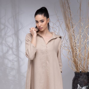 May include: A beige linen maxi dress with a collared neckline and long sleeves. The dress has a relaxed fit and a flowing silhouette.