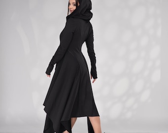 May include: A black hooded dress with a long, asymmetrical hemline. The dress has long sleeves and a fitted bodice. The model is wearing black boots.