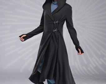 May include: A long-sleeved black hooded coat featuring a high-low hemline, thumbhole cuffs, and two silver-toned metal buckle closures on the front. The garment is worn over a blue turtleneck top and blue jeans, paired with black lace-up boots.