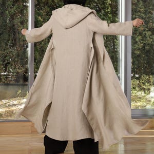 May include: A long, beige linen hooded coat with a tie belt. The coat is flowing and has a relaxed fit.