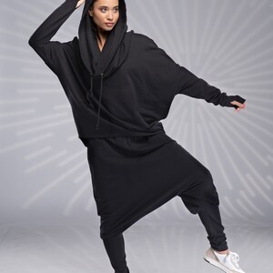 Puede incluir: Una sudadera con capucha negra y pantalones a juego con un corte holgado y fluido. La sudadera tiene una capucha con cord&oacute;n y los pantalones tienen una pierna ancha.