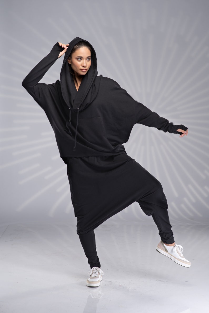 Puede incluir: Una sudadera con capucha negra y pantalones a juego con un corte holgado y fluido. La sudadera tiene una capucha con cord&oacute;n y los pantalones tienen una pierna ancha.