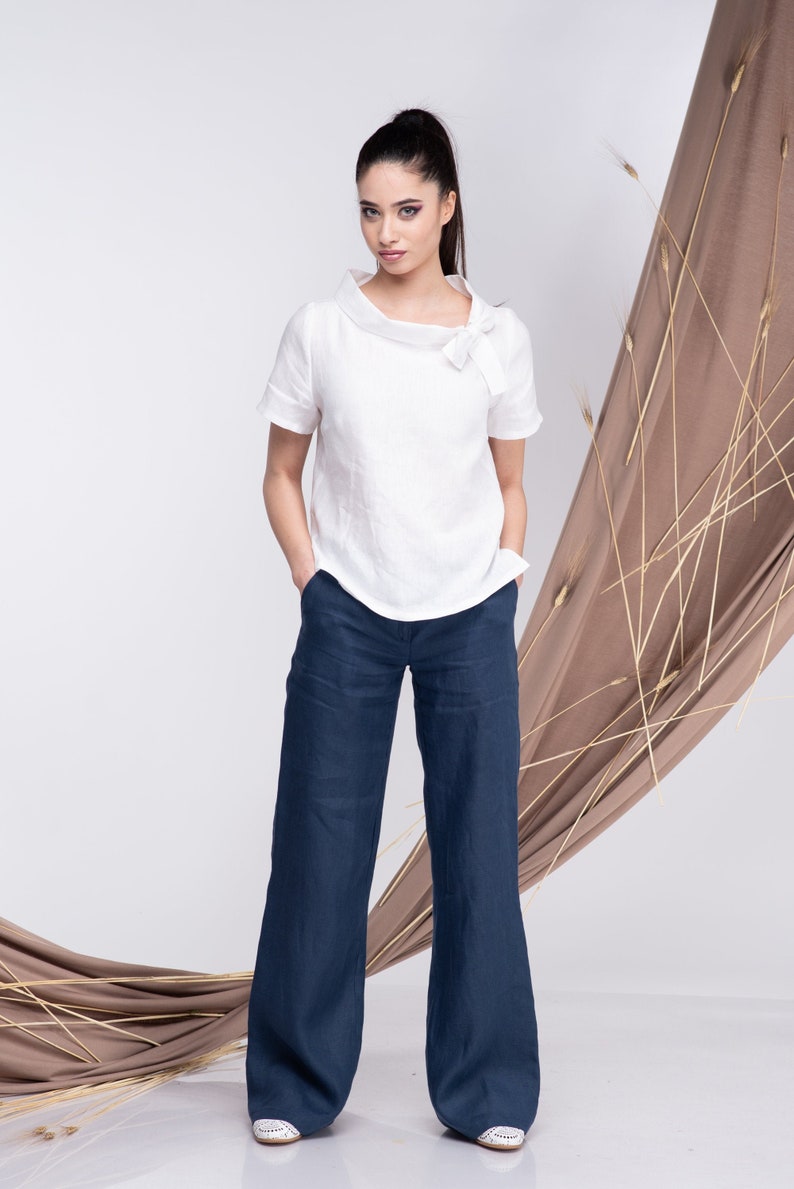 May include: A white linen top with a bow detail at the neckline, paired with dark blue wide-leg linen trousers.