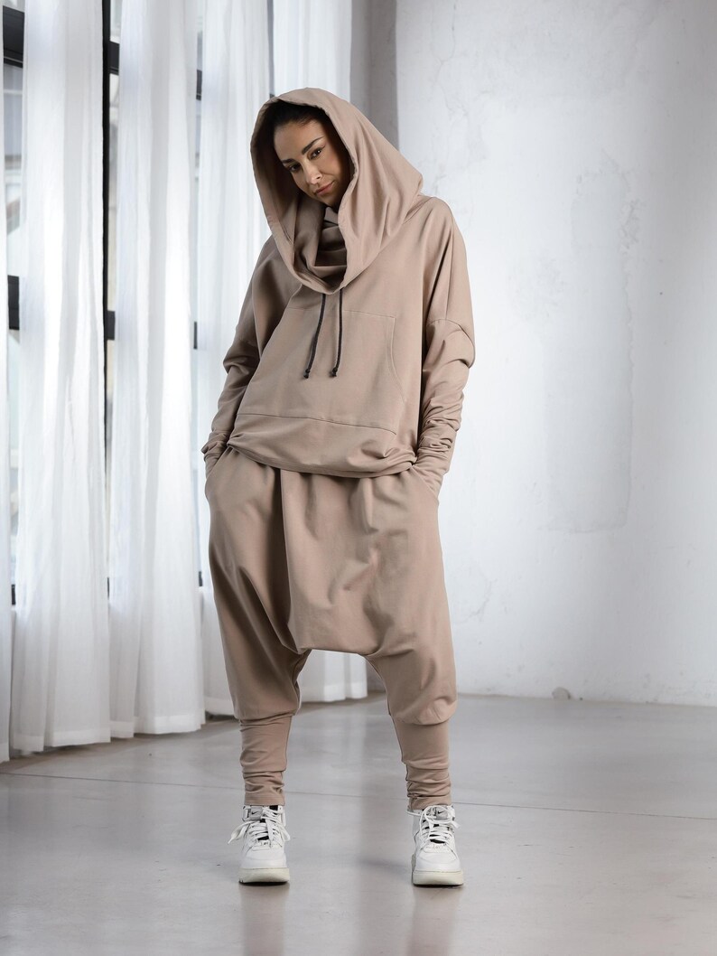 K&ouml;nnte beinhalten: Ein beiger Kapuzenpullover und eine passende Hose mit Kordelzug. Der Pullover hat einen Schalkragen und die Hose ist locker geschnitten mit weitem Bein.