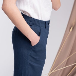 May include: A pair of dark blue linen trousers with a front pocket. The trousers have a relaxed fit and a wide leg.