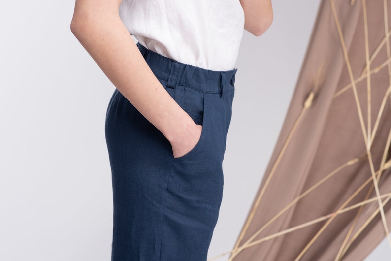 May include: A pair of dark blue linen trousers with a front pocket. The trousers have a relaxed fit and a wide leg.
