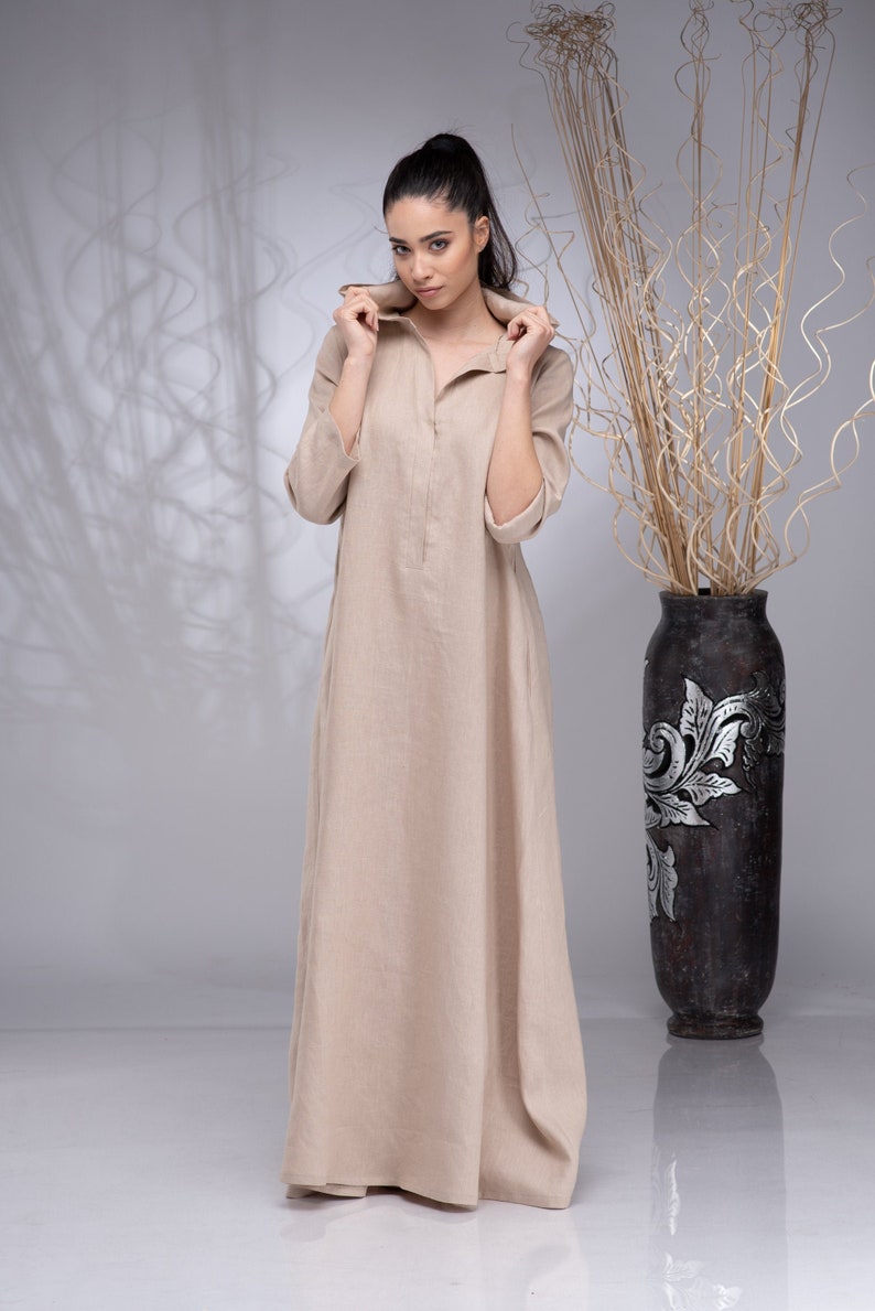 May include: A beige linen dress with a long, flowing skirt and a collar that can be worn up or down.