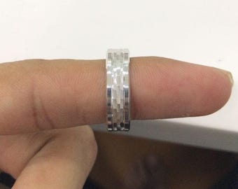 May include: A silver ring with a textured, geometric design. The ring is shown on a finger, with a close-up view highlighting the intricate pattern. The ring appears to be made of a shiny metal, reflecting light.