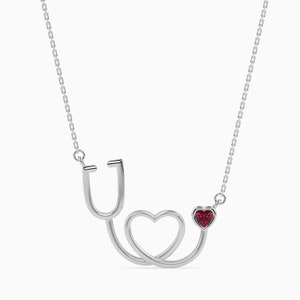 May include: Silver necklace with a stethoscope and a red heart charm. The stethoscope is shaped like a heart.