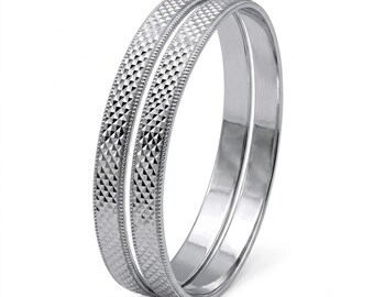 Può includere: Una coppia di bracciali rigidi in metallo color argento con una fascia centrale testurizzata a motivo di diamante, bordata da bordi lisci e perlati. I bracciali presentano una finitura lucida e riflettente e una forma circolare.