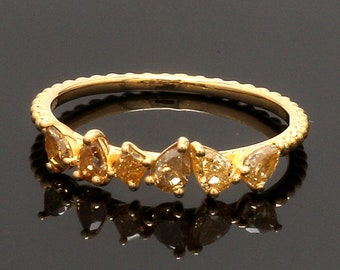 May include: A gold ring featuring a series of pear-shaped, amber-colored gemstones. The ring has a textured band and is set against a dark background, with the gemstones reflecting light.