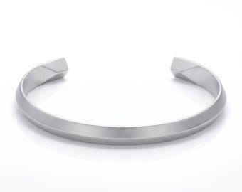 May include: A silver-toned metal cuff bracelet featuring a smooth, polished finish and a distinct angular, faceted design along the outer edge. The bracelet has an open-ended construction with tapered, flat ends, creating a clean, geometric silhouette.