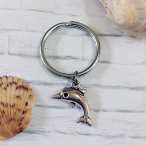 May include: Silver dolphin keychain with a silver key ring. The dolphin is jumping out of the water.