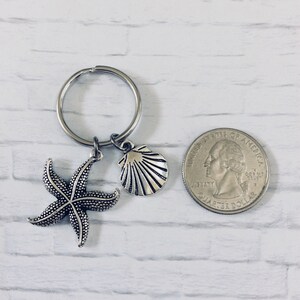 以下が含まれることがあります： スターフィッシュと貝殻のチャームが付いたシルバーキーチェーン。キーチェーンはシルバーキーリングに取り付けられています。キーチェーンはアメリカの25セント硬貨と同じくらいの大きさです。