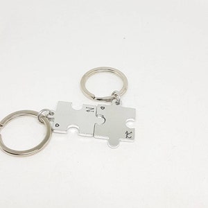 May include: Silver puzzle piece keyring with the letters "N" and "K" engraved on each piece. The pieces are connected by a silver ring.