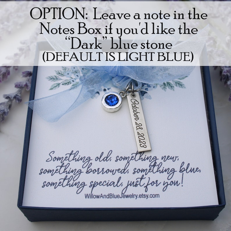 Op de afbeelding: Marineblauwe geschenkdoos met lichtblauw lint en zilveren bedel met blauwe steen en gegraveerde tag "October 28, 2023". De doos bevat een kaart met de tekst "Something old, something new..." en de Etsy shopnaam.